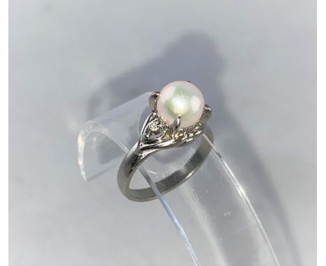 A white metal dress ring set with a pearl flanked by a small diamond to each shoulder, stamped 'PT900', size 'L-M', 5.4 gm 