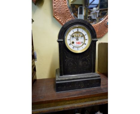 A late 19th century slate mantel clock, the circular enamel dial with exposed escapement, with engraved decoration and confor