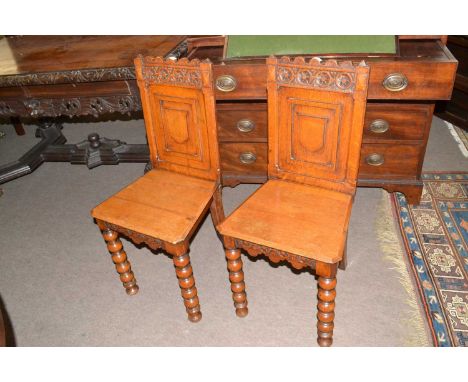 A pair of Victorian oak hall chairs with shield decorated panel backs, plain seats and bobbin turned front legs, 88cm high