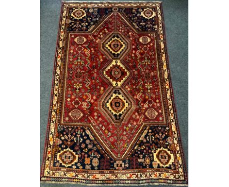 A Persian Qashgai rug / carpet, triple medallion centre within a field woven with stylised flowers in tones of red, cream, an