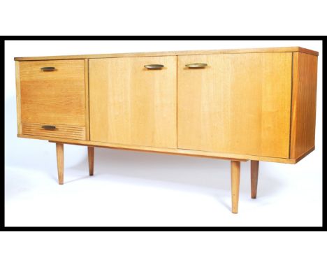 A 1970's retro light teak wood sideboard of low and long form being raised on tapering legs having a series of drawers and cu