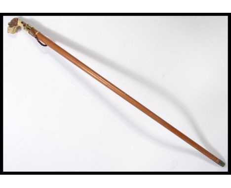 A vintage 20th century walking stick cane having a tapering wooden shaft with brass collar and the handle in the form of a Ai