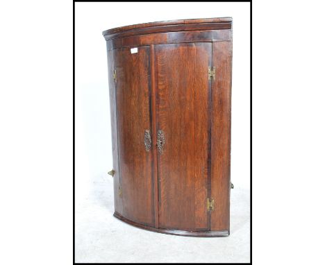 A Georgian 19th century hanging bow fronted oak corner cabinet having flared cornice over twin full length panel doors with s