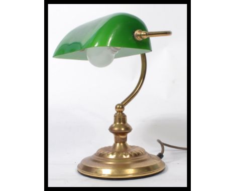A vintage 20th century bankers desk lamp having an adjustable green glass shade raised on a brass support and circular base.