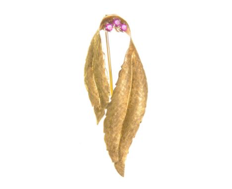 A ruby brooch
Three circular-cut rubies set between two chased gold leaves, stamped 750, height 4.7cm 
