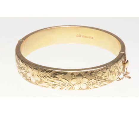 A 9ct gold bangle
One side engraved with foliate decoration, with hinge and safety chain, length 6.8cm, weight 20g
