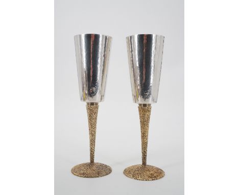 Stuart Devlin A pair of Elizabeth II silver champagne flutes, each with a tapering cylindrical bowl, planished and parcel-gil