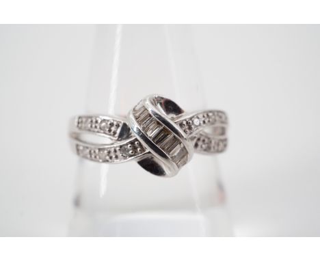 A contemporary 9ct white gold and diamond cocktail ring, having two parallel diamond set ribbons culminating in a baguette-cu