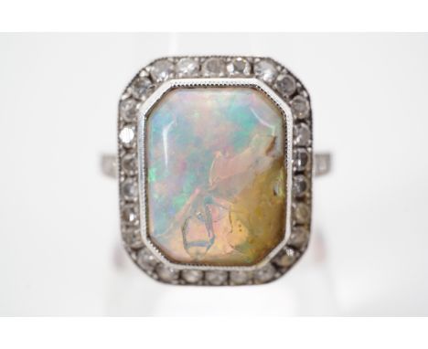 A precious white metal and opal dress ring, of Art Deco influence, having a central opal cabochon with canted corners, milleg