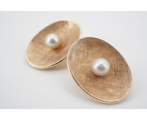 A pair of high carat yellow metal and pearl ear clips, each of oval section and dished form, textured and centrally set with 