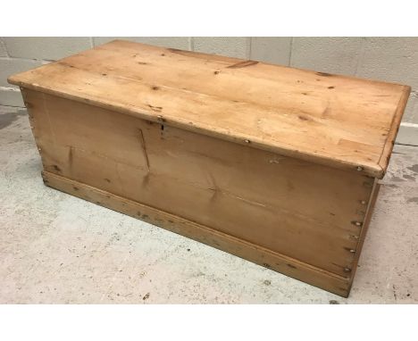 A Victorian waxed pine trunk of plain form, the top opening to reveal a candle box, raised on a plinth base, 110 cm wide x 48