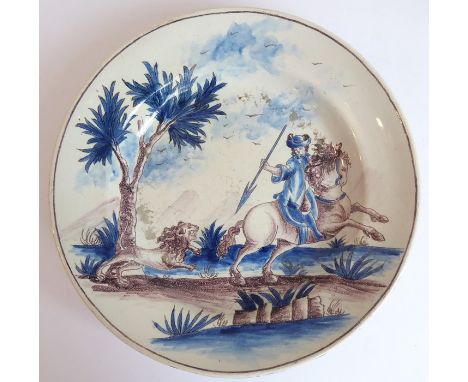 A 19th century Delftware dish hand-decorated with a mounted male figure about to spear a chasing lion (23.5cm diameter)
