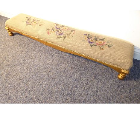 A long footstool having floral needlework tapestry top and gilt-style base on bun feet (127cm wide)