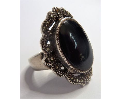 A silver ring centrally set with a vertical oval cabochon black hardstone within a marcasite-mounted border
(The cost of&nbsp