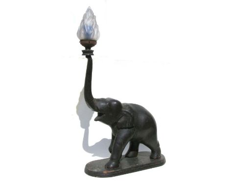 A large ebonised table lamp in the form of an elephant with an upraised trunk having a frosted glass flame shade, overall 92c