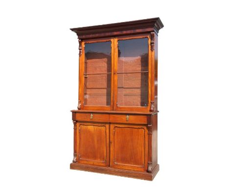 An early 19th century mahogany bookcase on cupboard, the pair of glazed doors enclosing a shelved interior above two frieze d