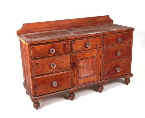 A Victorian pine dresser base with an arrangement of seven drawers and central cupboard, with later glass handles, on turned 