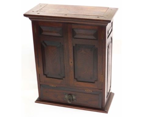 An early 20thC oak Arts &amp; Crafts smoker's cabinet, with panelled sides and doors, enclosing a single shelf, above a hinge