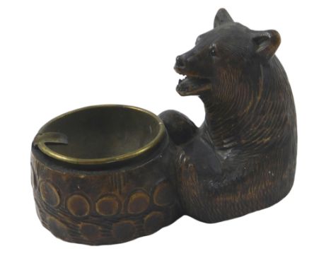 A Black Forest ashtray, carved in the form of a bear, with brass insert, 16cm long.