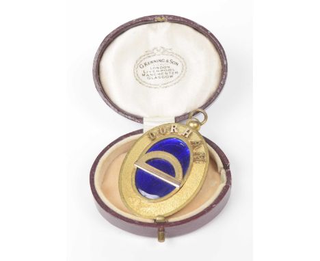 An oversized oval pendantIn gilt metal, depicting 'DURHAM' on the from, with blue enamel detail and a protractor, cased