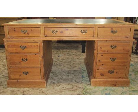 A stripped pine knee hole twin pedestal desk, with inset writing surface over an arrangement of nine frieze drawers and set o