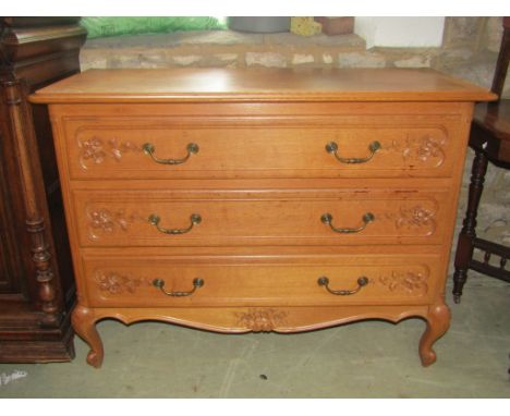 A medium to light oak three drawer commode, with carved foliate and moulded detail, brass drop handles, shaped apron and scro