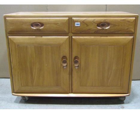 A light Ercol elm cottage side cupboard or small dresser base enclosed by a pair of panelled doors and two frieze drawers, to