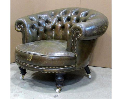 A late Victorian low green leather, upholstered tub chair with scrolled and buttoned back, raised on ebonised turned forelegs