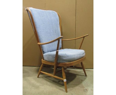 An Ercol medium to light beechwood Windsor winged and stick-back armchair, with swept arms, loose cushions, splay turned legs