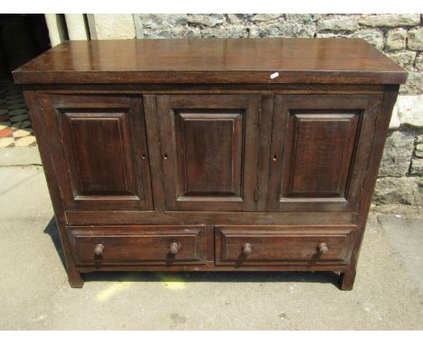 An Old English style low oak side cupboard partially enclosed by three fielded panelled doors over two drawers together with 
