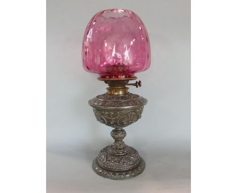 A Victorian cast spelter oil lamp with richly detailed frame work, complete with cranberry glass shade and twin burner 