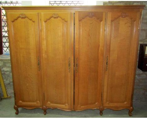 A light oak armoire enclosed by four full length fielded arched panelled doors over a shaped apron and squat scrolled cabriol