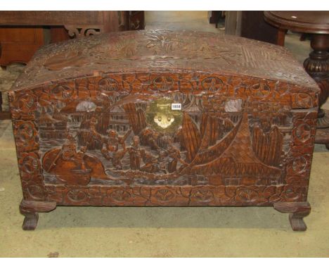 An Eastern camphor wood domed top chest with profusely carved detail, brass lock plate and lasp and raised on shaped bracket 