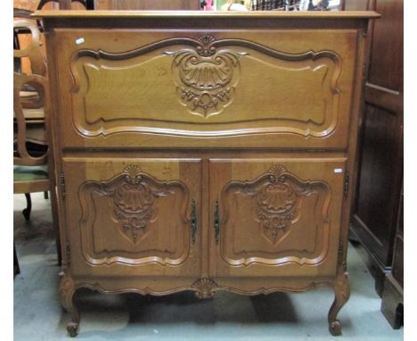 A medium to light oak side cupboard, freestanding and enclosed by three moulded and fielded panelled doors with carved acanth
