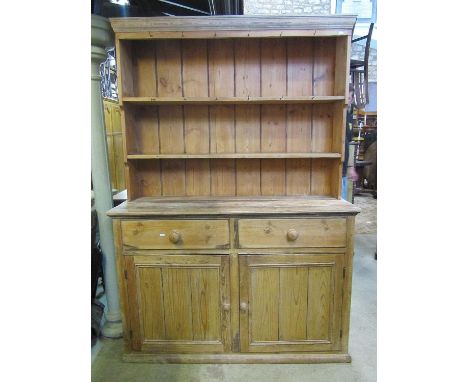 A stripped pine farmhouse kitchen dresser, the base enclosed by a pair of panelled doors beneath two frieze drawers and reces
