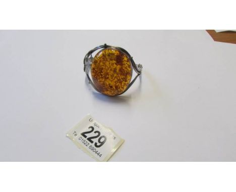A silver bangle with large amber coloured stone.