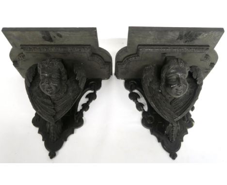A PAIR OF 19TH CENTURY EBONISED WALL BRACKETS with shaped moulded tops over carved cherubs heads flanked with wings over shap