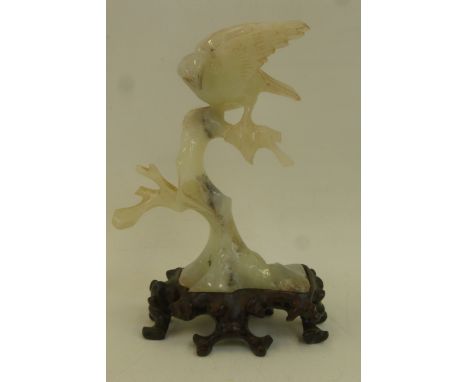A white jade carving of a bird in a tree, raised on a carved wooden stand, signed to the base of the jade.