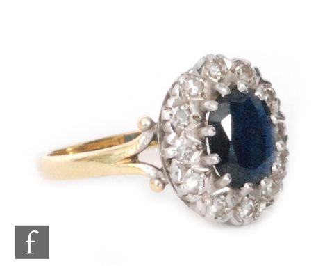 An 18ct hallmarked sapphire and diamond cluster ring, central oval sapphire within a diamond surround to split shoulders, rin