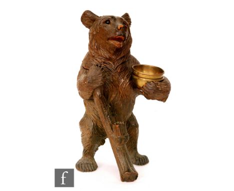 A Black Forest carved tobacco jar in the form of a bear standing holding a bough and a brass bowl, inset glass eyes, height 3