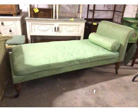 A late 19thc/early 20thc daybed, in green floral damask fabric, with rolled back bolster cushion, on turned supports terminat