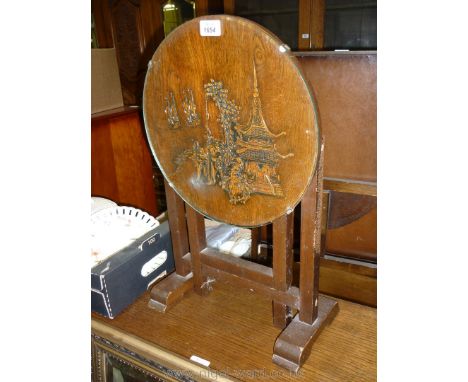 A dark Oak framed metamorphic Fire screen/table having a folding circular top with Chinoiserie scene of a pavilion, storks an