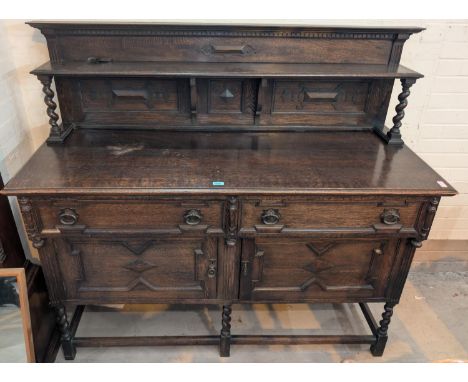 A 1930's large heavy oak carved sideboard with raised back, barley twist supports drawers and cupboards bellow