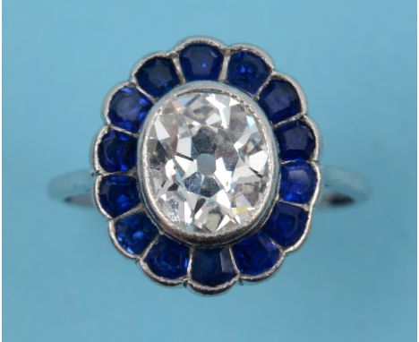 A diamond and sapphire flowerhead ring, the centre opal diamond surrounded by shaped sapphire petals, in a white coloured met