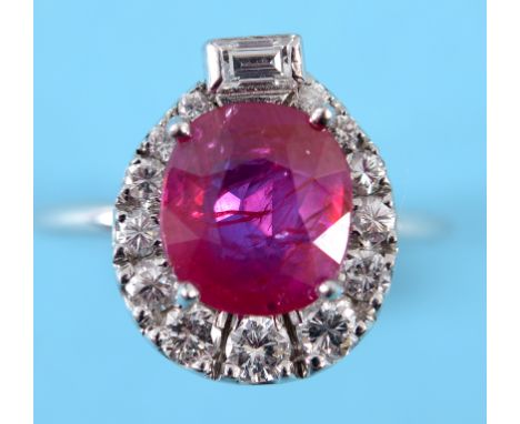 A white coloured metal ruby and diamond cluster ring, the central cushion cut ruby surrounded by brilliant and a baguette cut