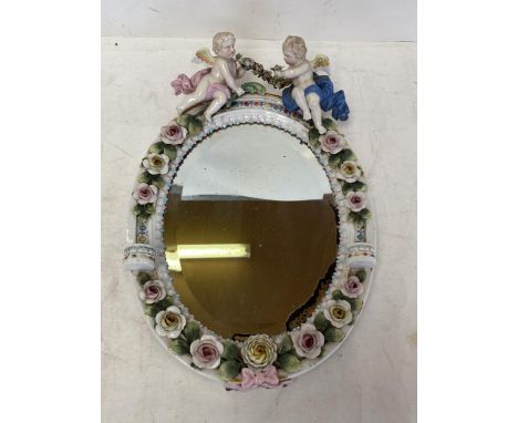 A pair of circular hanging wall mirrors set in a ceramic oval frame with floral decoration surmounted by two cherubs 