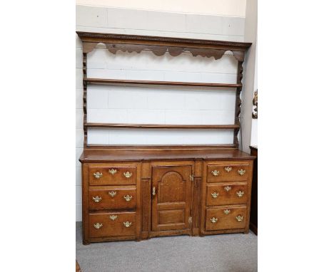 An Oak Dresser and Rack, 18th century, the inverted breakfront base with a central arch panel door flanked by two sets of thr