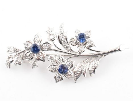 A white gold, diamond and sapphire brooch pin. The white gold brooch pin in the form of a floral spray set with twenty five g