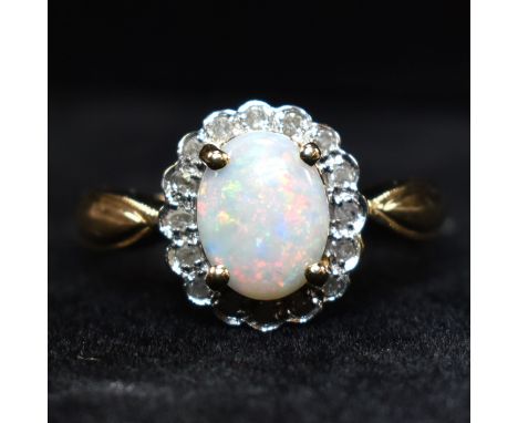 A hallmarked 9ct gold, opal and diamond cluster ring. The 9ct yellow gold ring having a central four claw set oval opal caboc