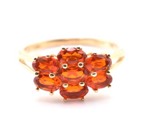 A hallmarked 9ct gold and fire opal cluster ring. The 9ct yellow gold ring having seven east-west set oval cut fire opals to 